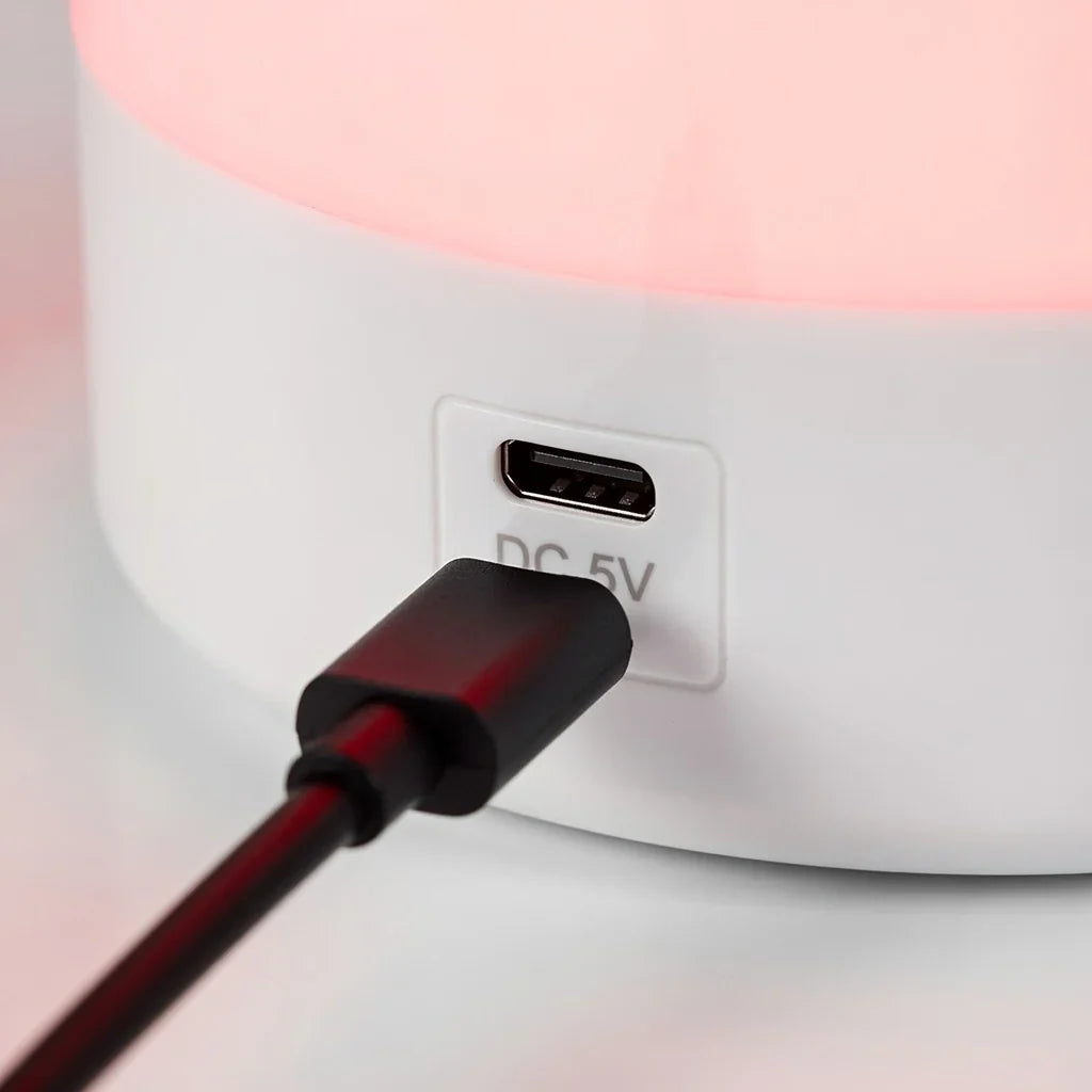 Close-up of a USB charging cable plugged into a white red light lamp base, glowing softly