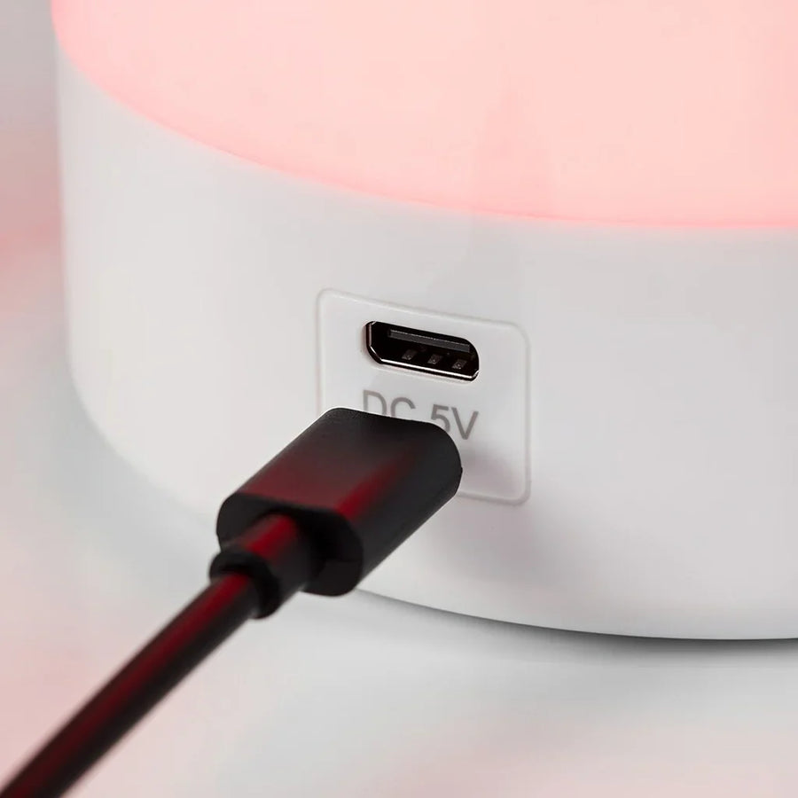 Close-up of a USB charging cable plugged into a white red light lamp base, glowing softly