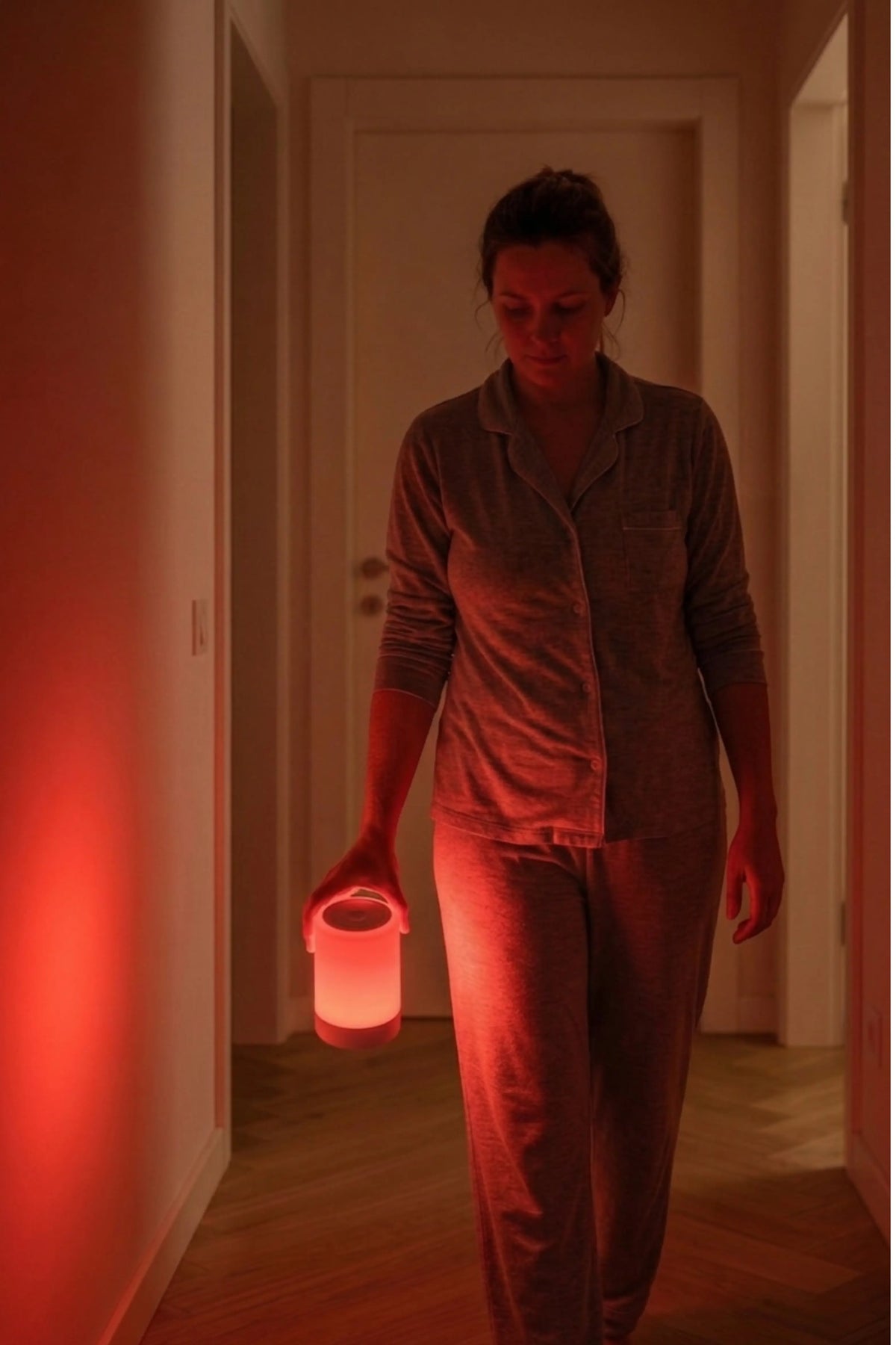 Person walking down a dimly lit hallway holding a small light source.
